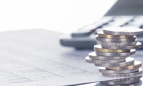 service-finanzierung Harbeke • Stapel von Münzen neben einem Taschenrechner und Finanzdokumenten.