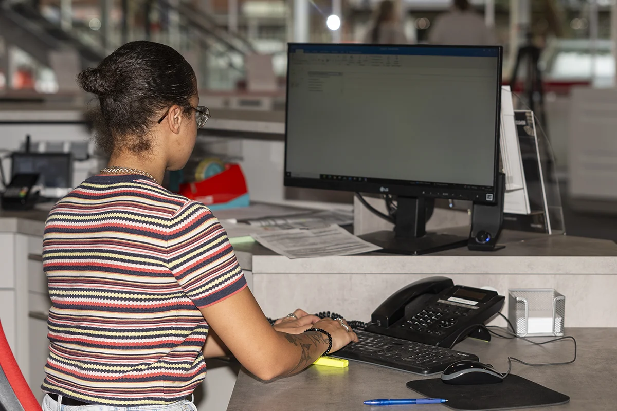 harbeke-beratung Harbeke • Person arbeitet am Computer im Büro, Telefon und Unterlagen sichtbar.